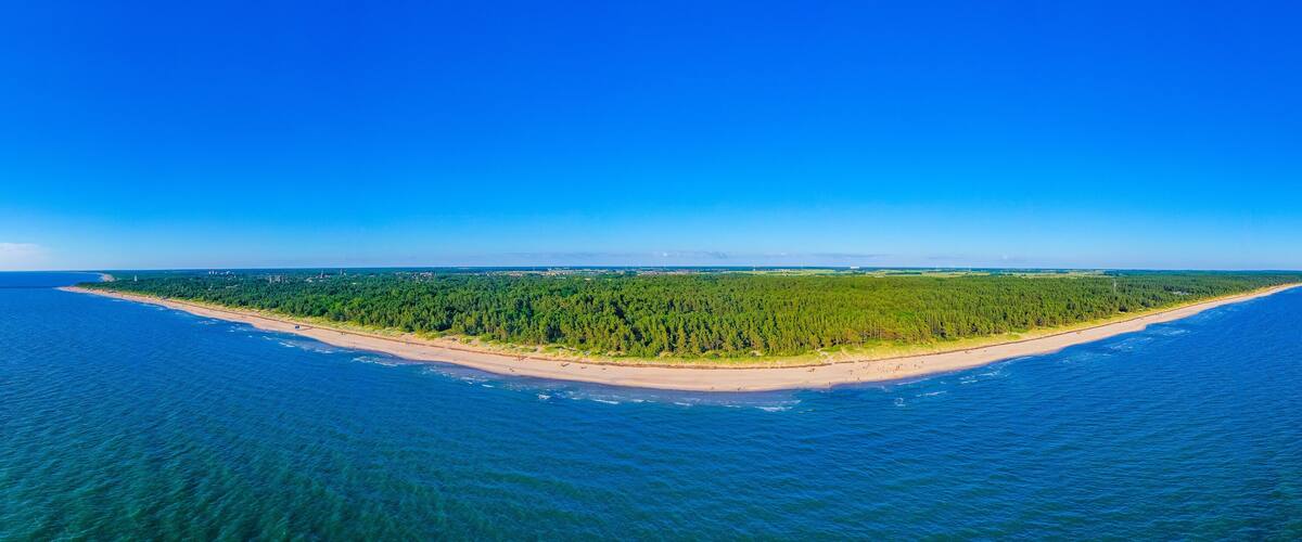 An aerial view of a narrow island with a beach and dense forest.
