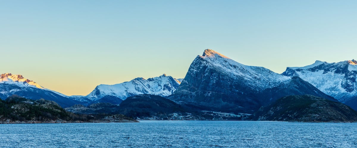 Snow-covered mountains, a calm lake, and a clear sky.