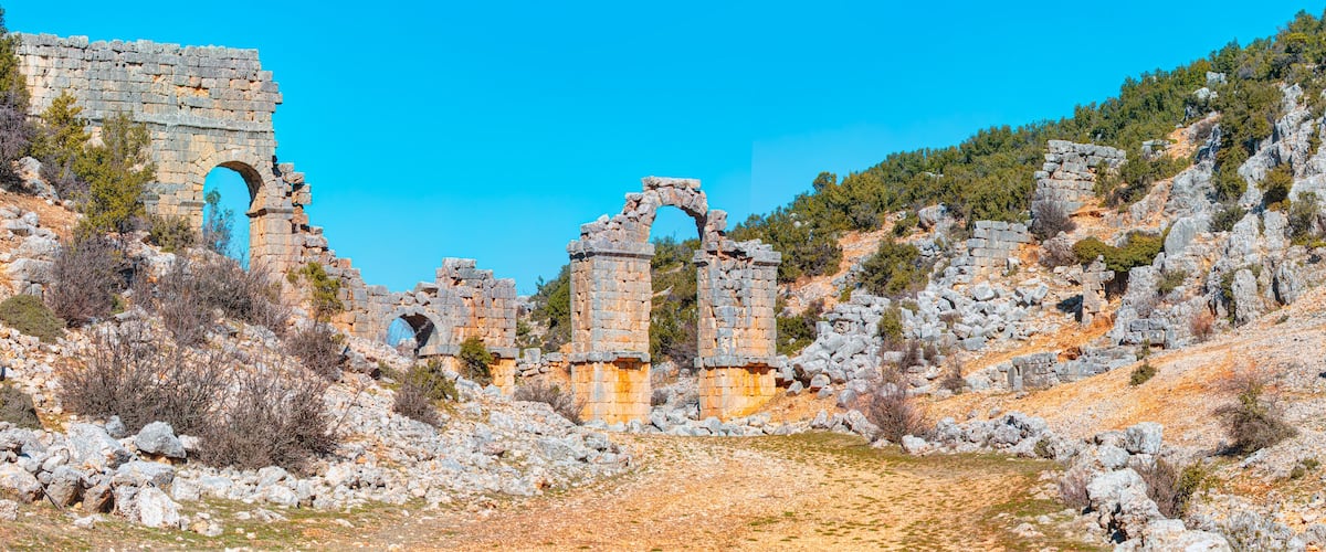 Ancient stone ruins with arches and walls amidst rocky terrain and sparse vegetation.