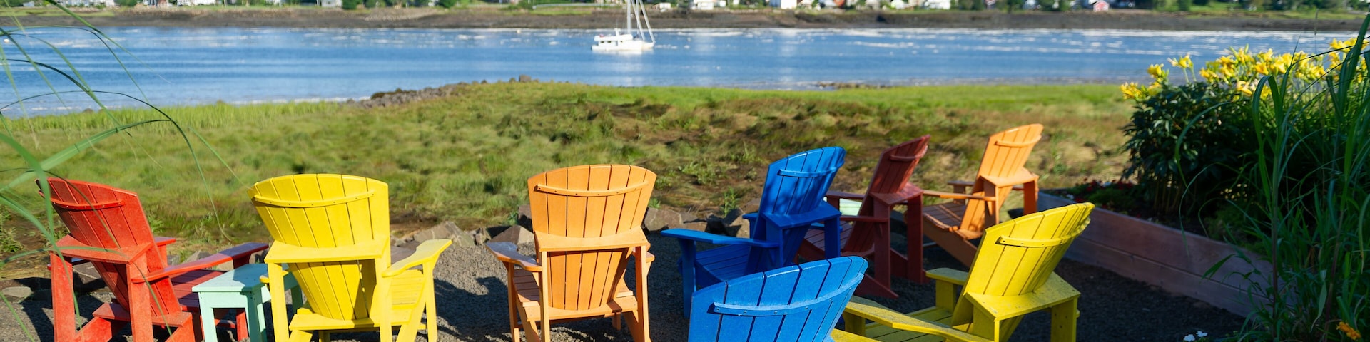Multicolor Adirondack chairs facing the calm water of the Bay of Fundy in Nova Scotia, Canada on a beautiful summer day