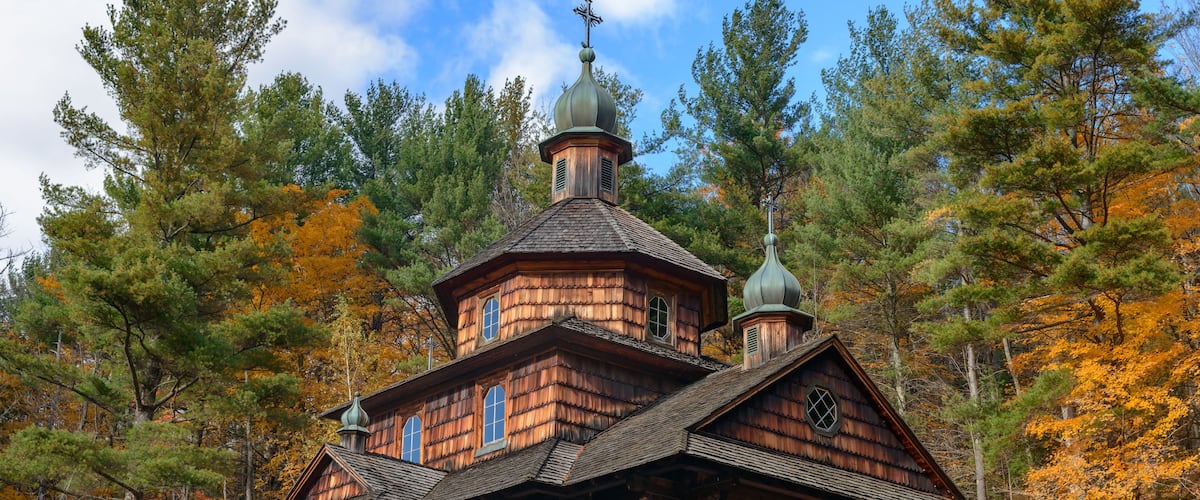 A wooden church with a bell tower surrounded by autumn trees.