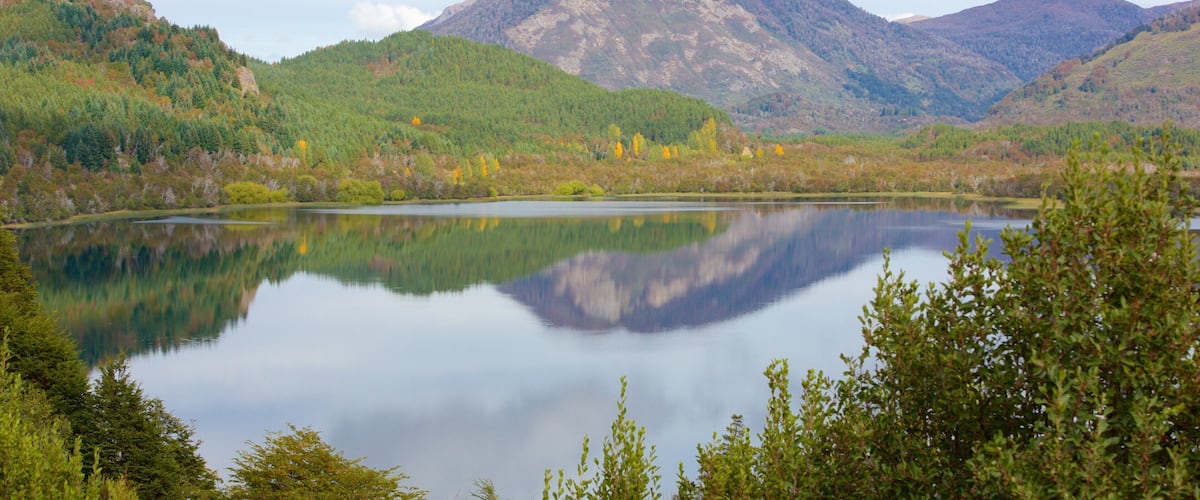 A calm lake surrounded by forested hills and a mountain in the background.