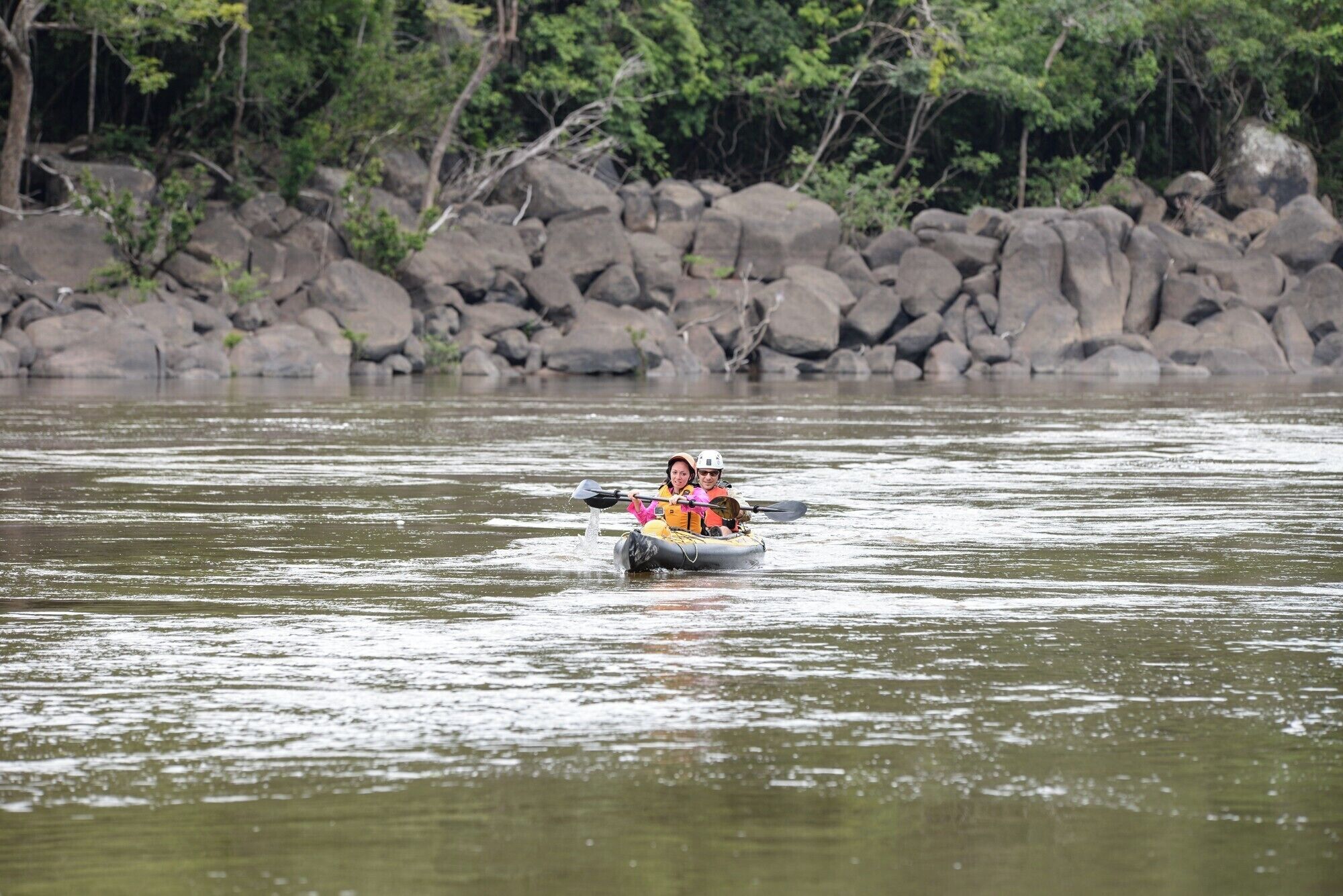 A person kayaking on a river surrounded by rocks and trees.