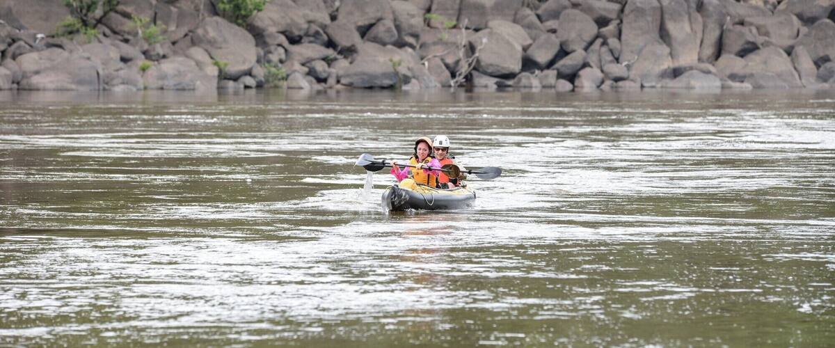 A person kayaking on a river surrounded by rocks and trees.