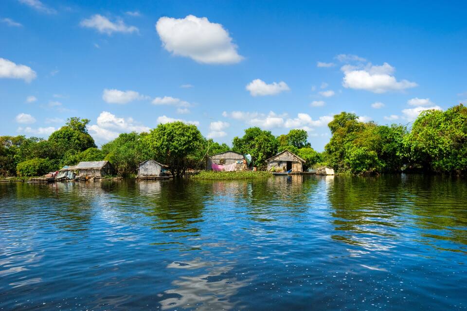 A calm river with houses on stilts, surrounded by lush greenery and a clear blue sky.