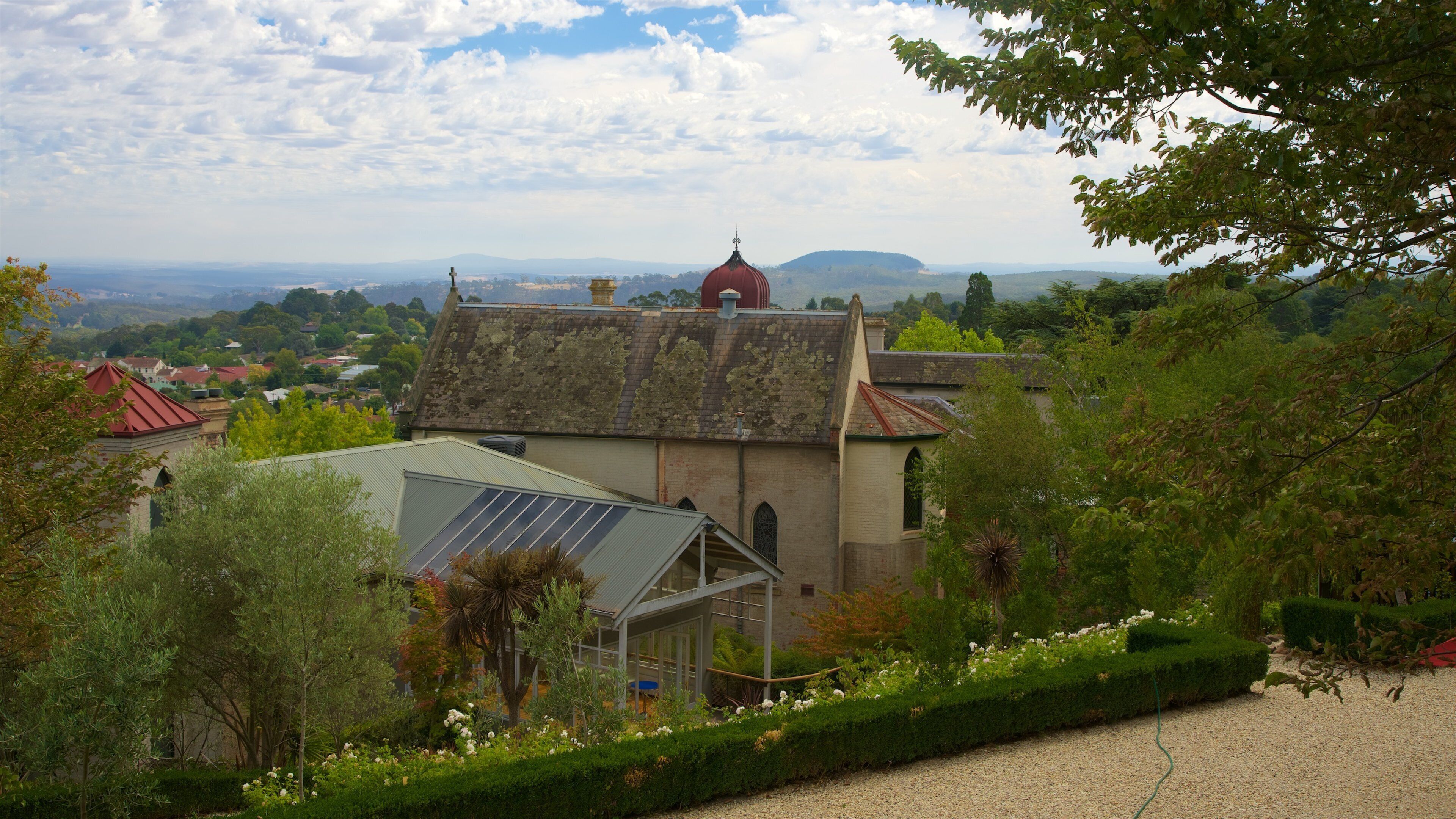 A church with a red dome, surrounded by lush greenery and a view of distant hills.