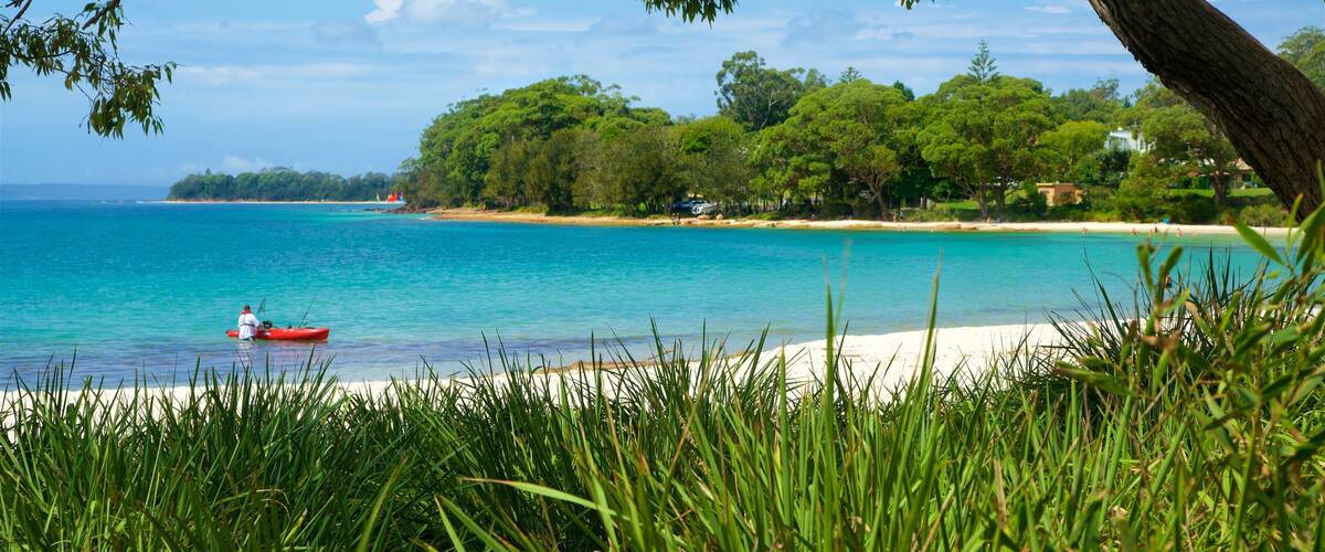 A beach with clear turquoise water, a red kayak, and lush greenery.