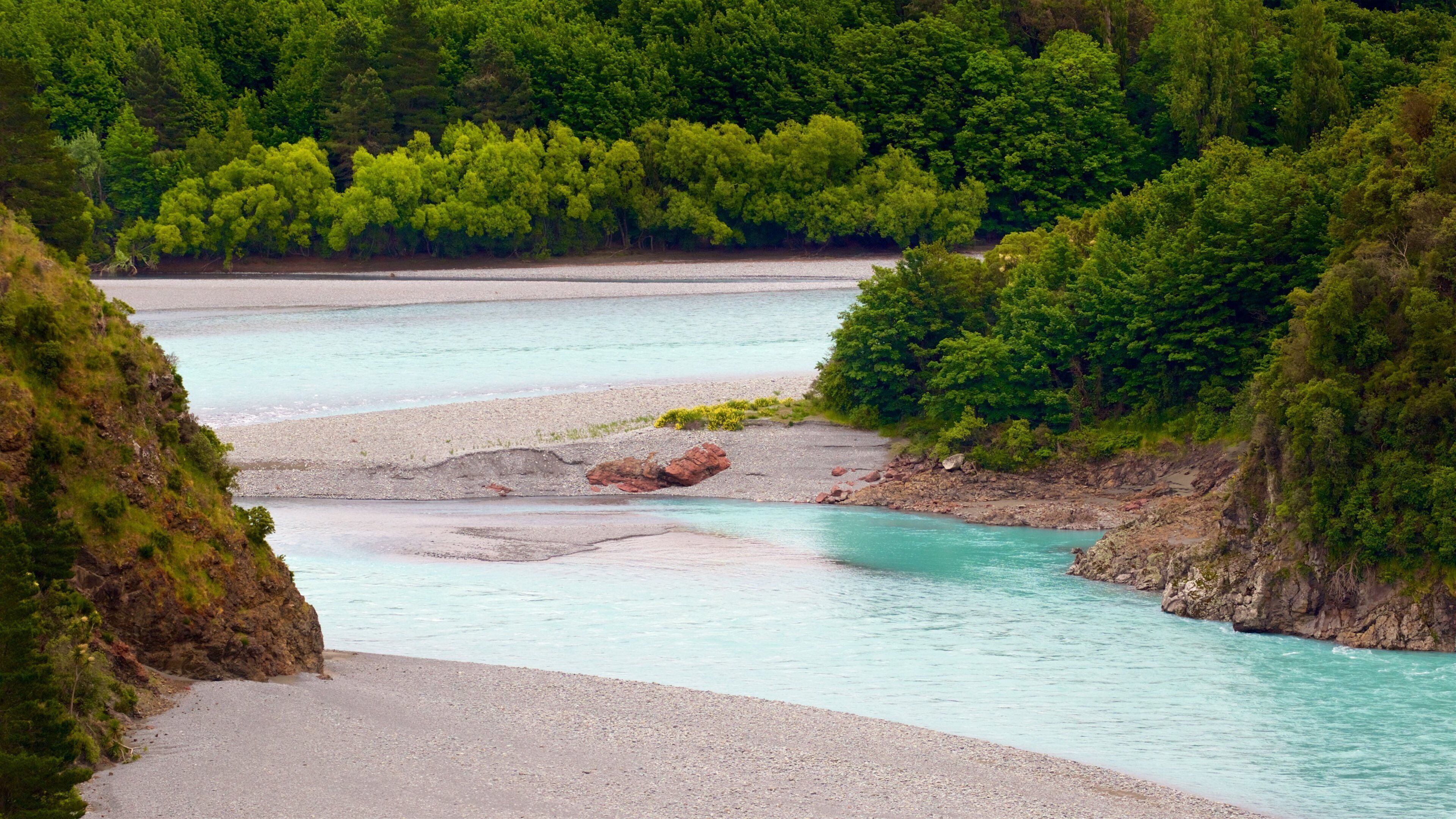 A river flowing through a forested valley with rocky banks and clear turquoise water.