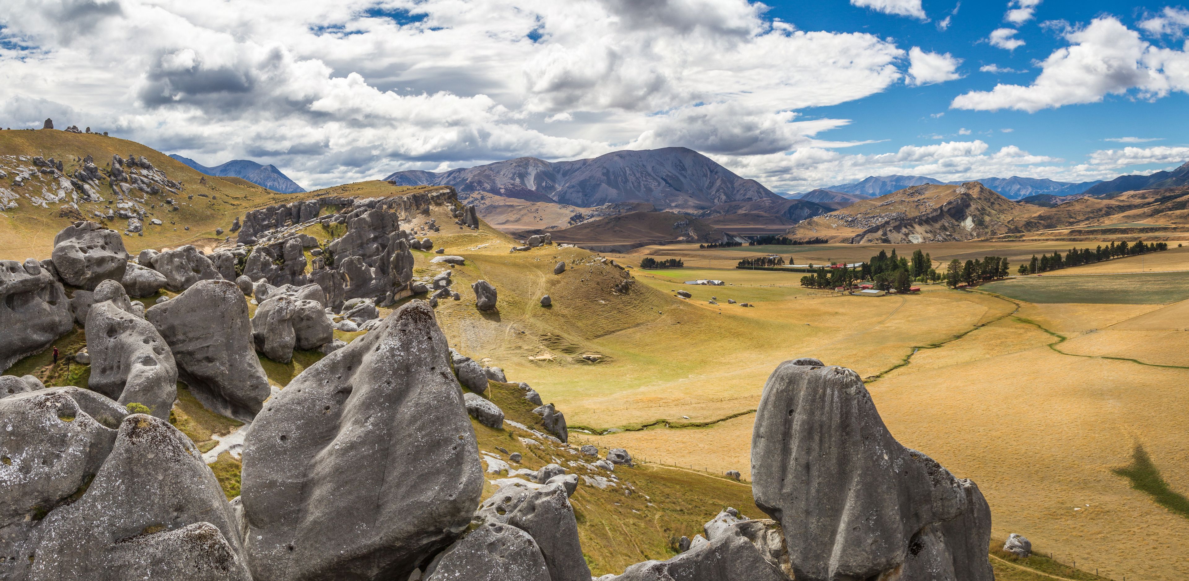 A mountainous landscape with large boulders, a valley, and distant mountains under a partly cloudy sky.