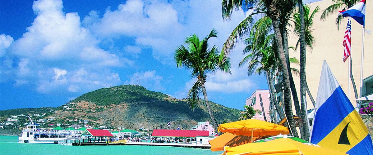 A beach with yellow lounge chairs, palm trees, a boat, and a pier.