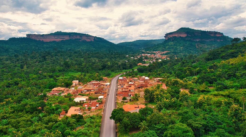 Aerial view of a road cutting through Atwea town and it's lush green vegetation, with Atwea Mountain peaks in the distance, Asuafu, Ashanti Region, Ghana.