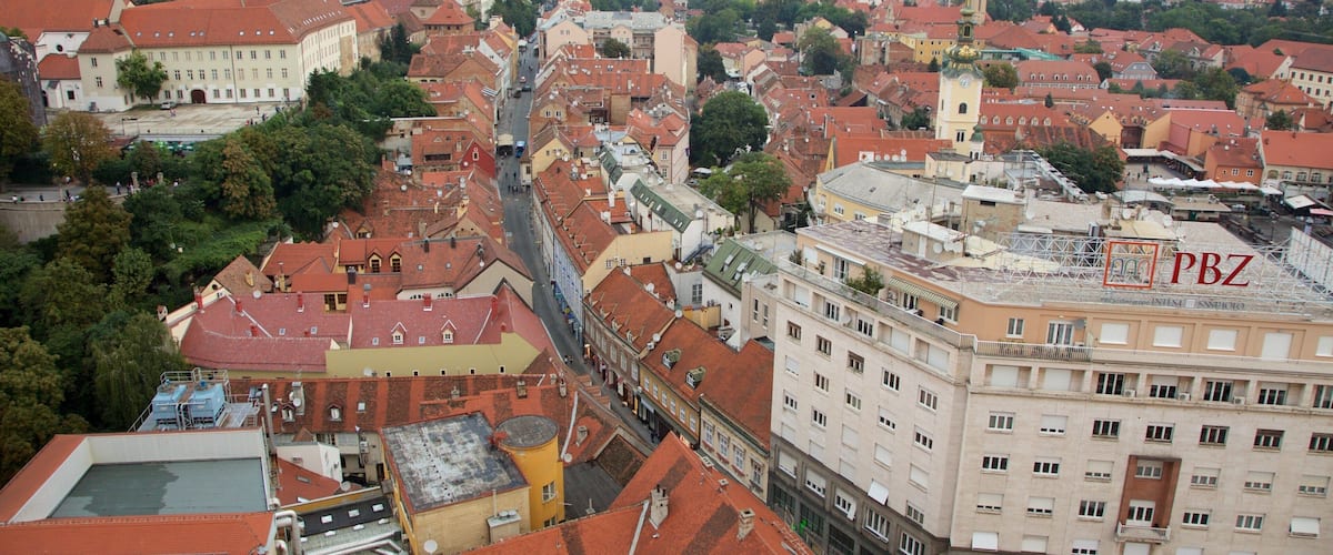 A cityscape with red-roofed buildings, a prominent tower, and a mountain range in the background.