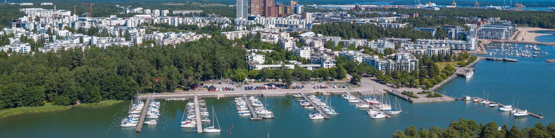A coastal cityscape with a marina filled with boats, surrounded by dense forests and urban buildings.