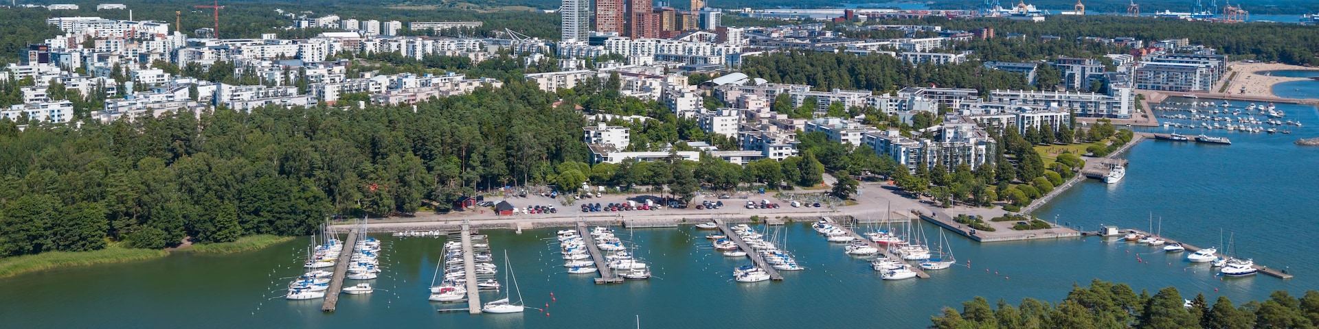Eine Küstenstadt mit einem Hafen voller Boote, umgeben von dichten Wäldern und modernen Gebäuden.