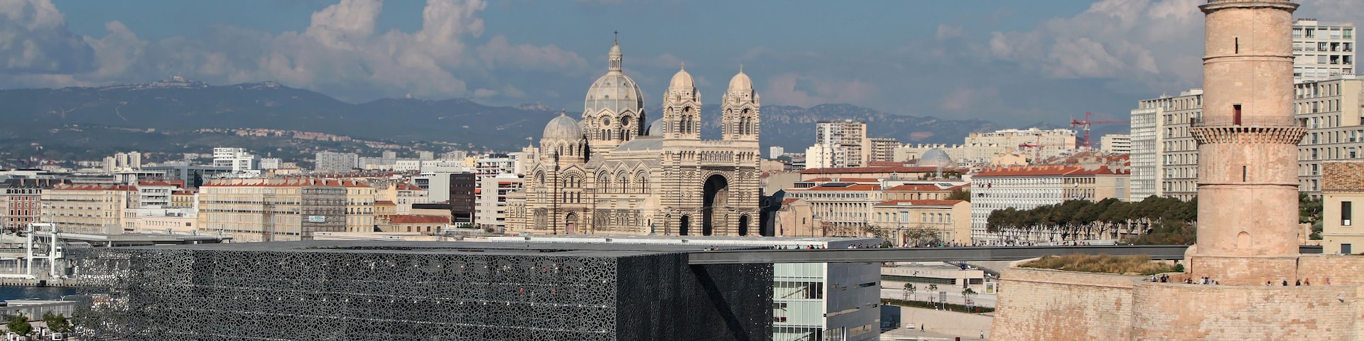 Un paisaje urbano costero con arquitectura histórica, una estructura moderna de vidrio y un faro.