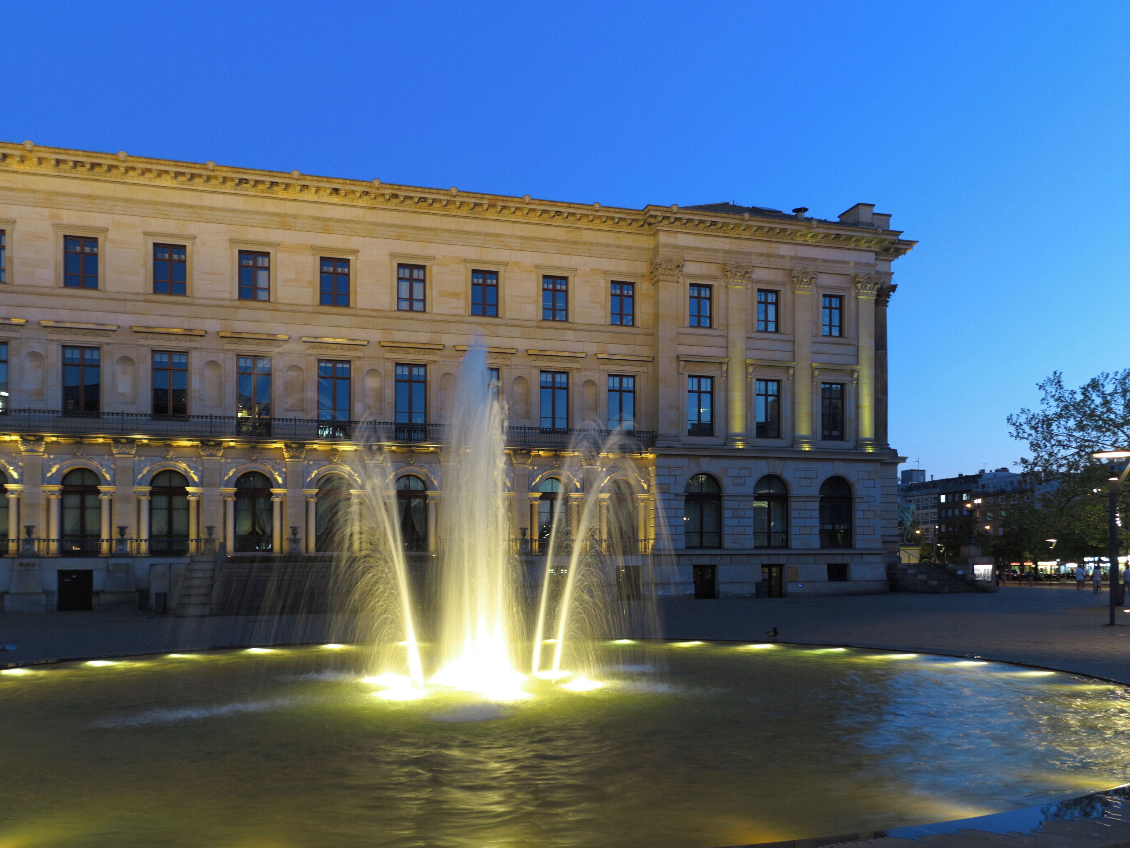 Ein historisches Gebäude mit einem Brunnen davor.