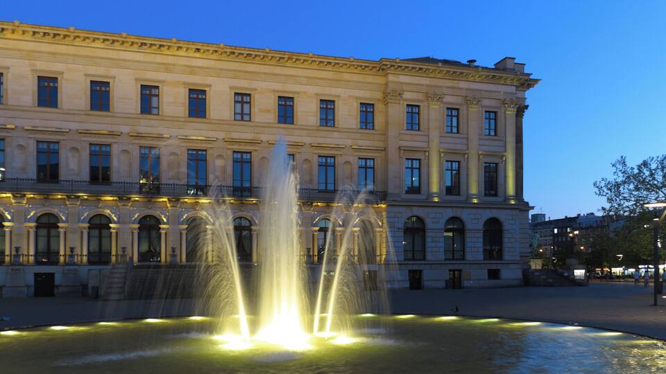 Ein historisches Gebäude mit einem Brunnen davor.