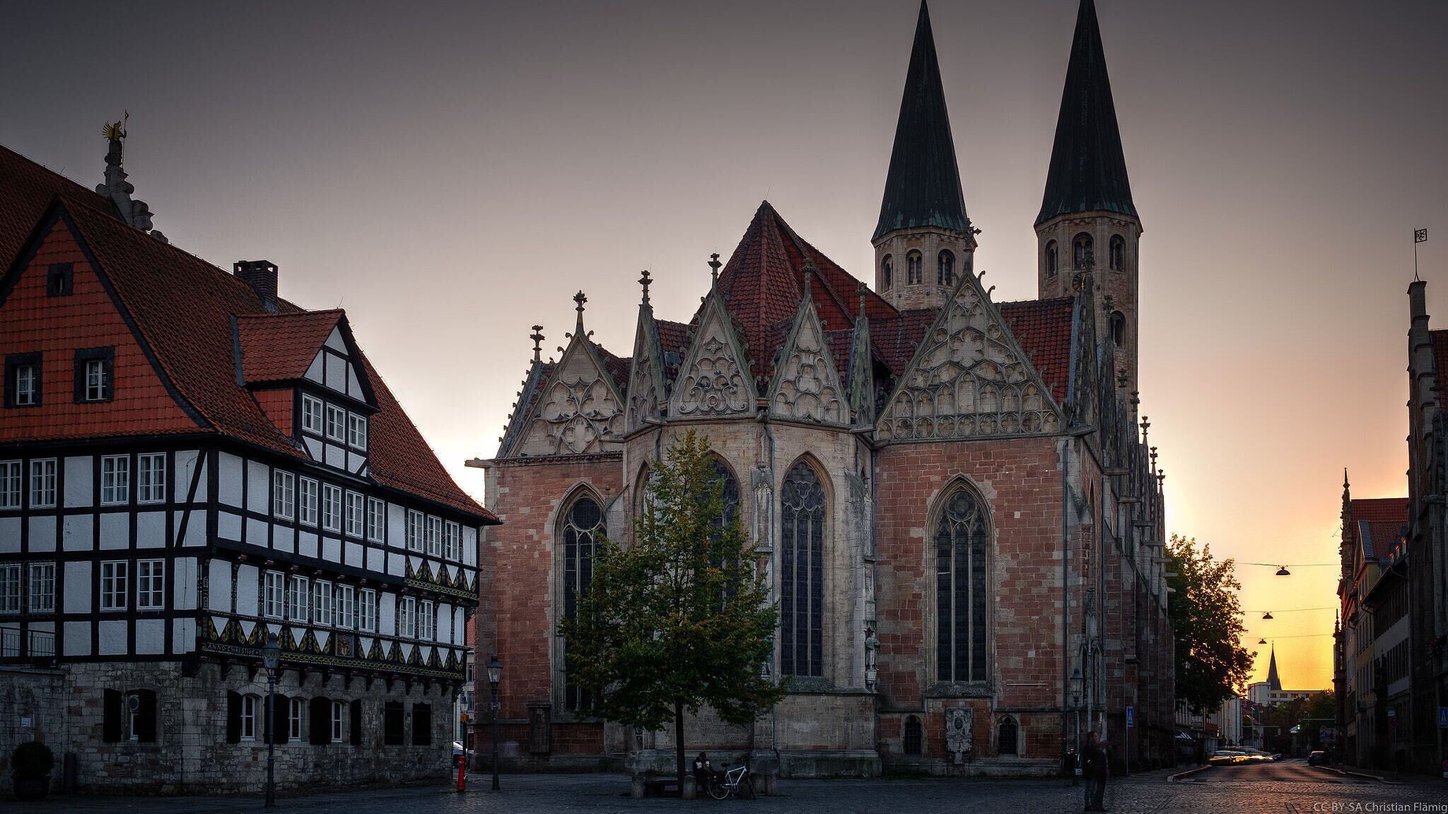 Eine historische Kirche mit zwei hohen Turmspitzen und ein traditionelles Fachwerkhäuschen in der Nähe.