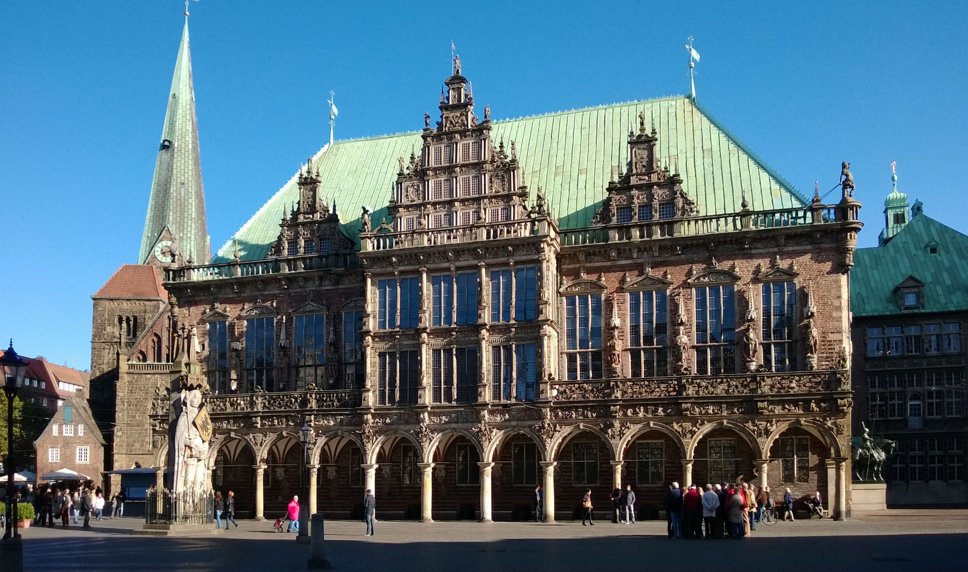 Un edificio histórico con arquitectura ornamentada, una torre del reloj y una estructura con techo verde.