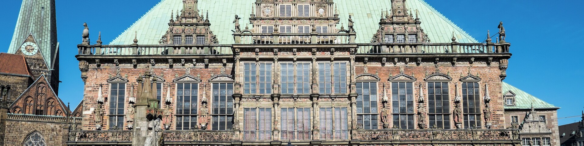 Un edificio histórico con arquitectura intrincada, una destacada torre del reloj y una amplia plaza abierta.
