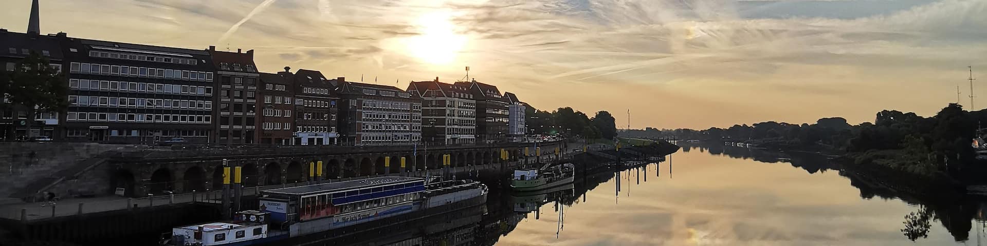 A river reflecting the sky with a sunset, buildings along the riverbank, and a boat.