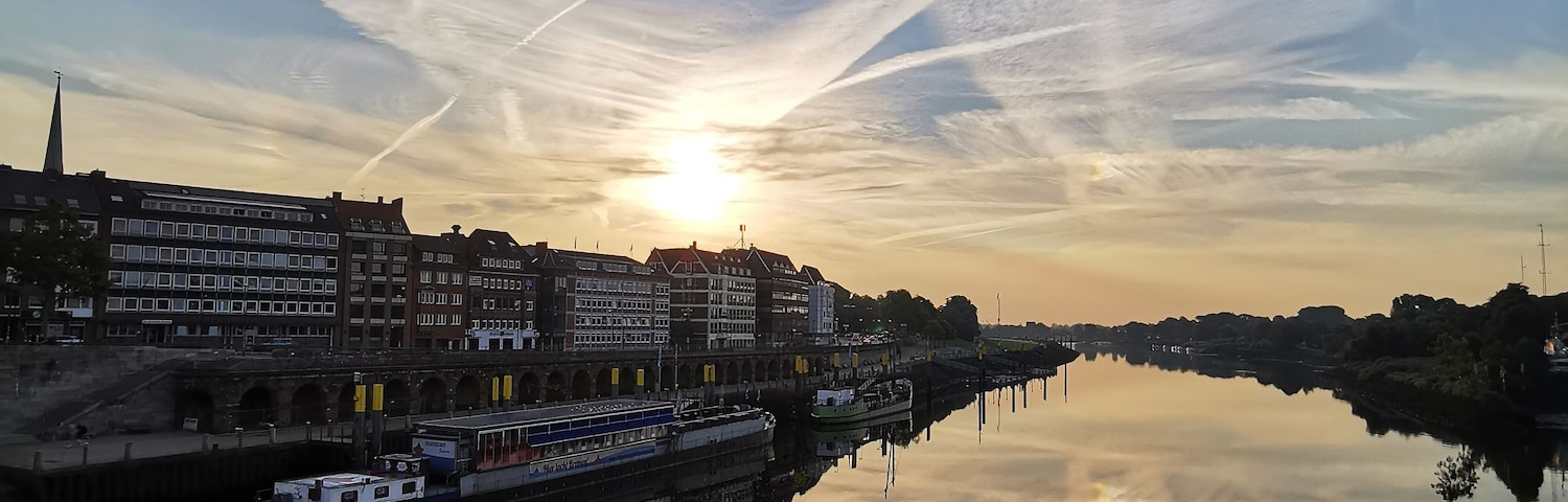 Une rivière qui reflète le ciel au coucher du soleil, des bâtiments le long de la rive et un bateau.