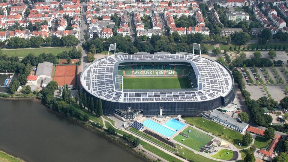 Une vue aérienne d’un stade où l’on peut lire les mots « WER DER BREMEN » sur le terrain, le tout étant entouré d’une rivière, d’immeubles résidentiels et d’une piscine.
