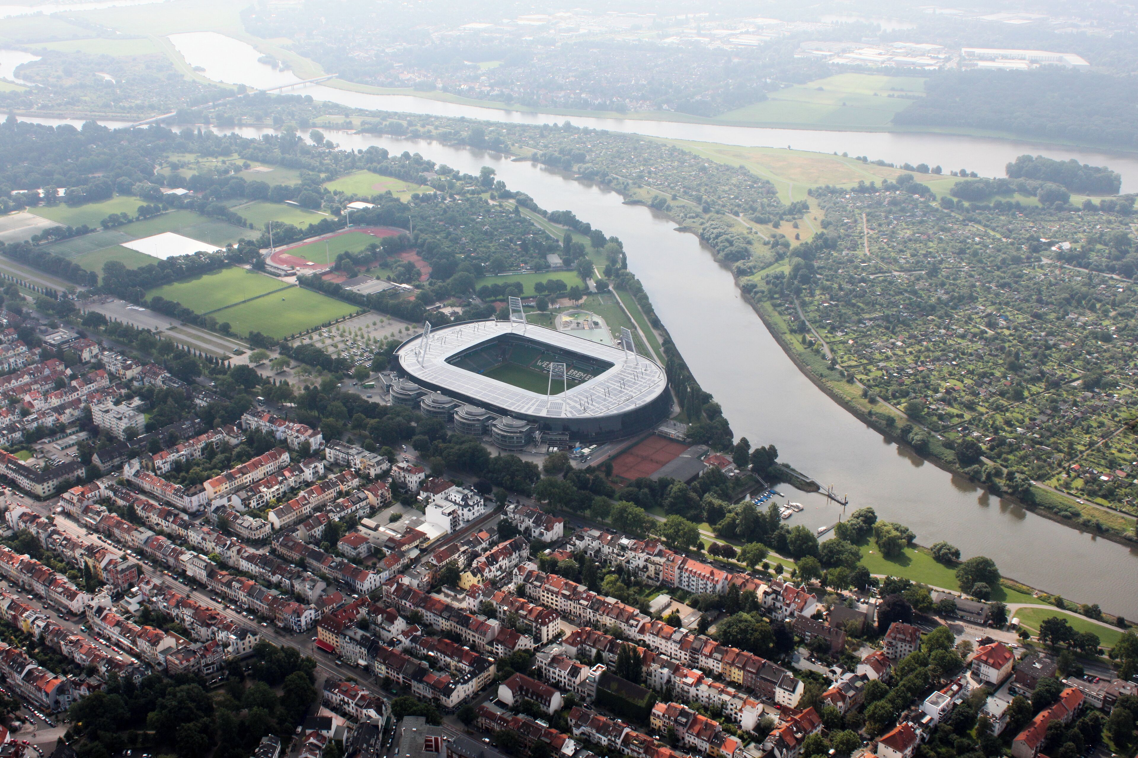 Vista aérea de una ciudad que muestra un estadio grande, un río y zonas residenciales circundantes.