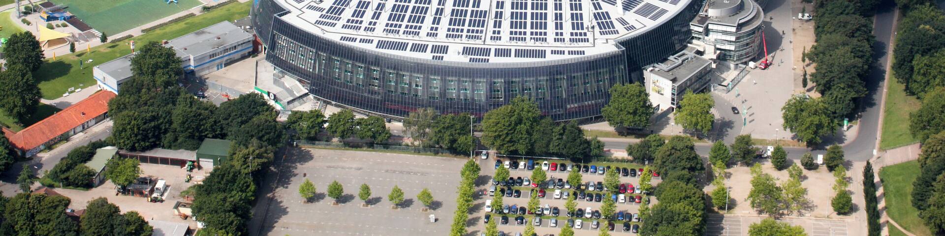 An aerial view of a stadium with a football field, surrounded by a river, trees, and residential buildings.