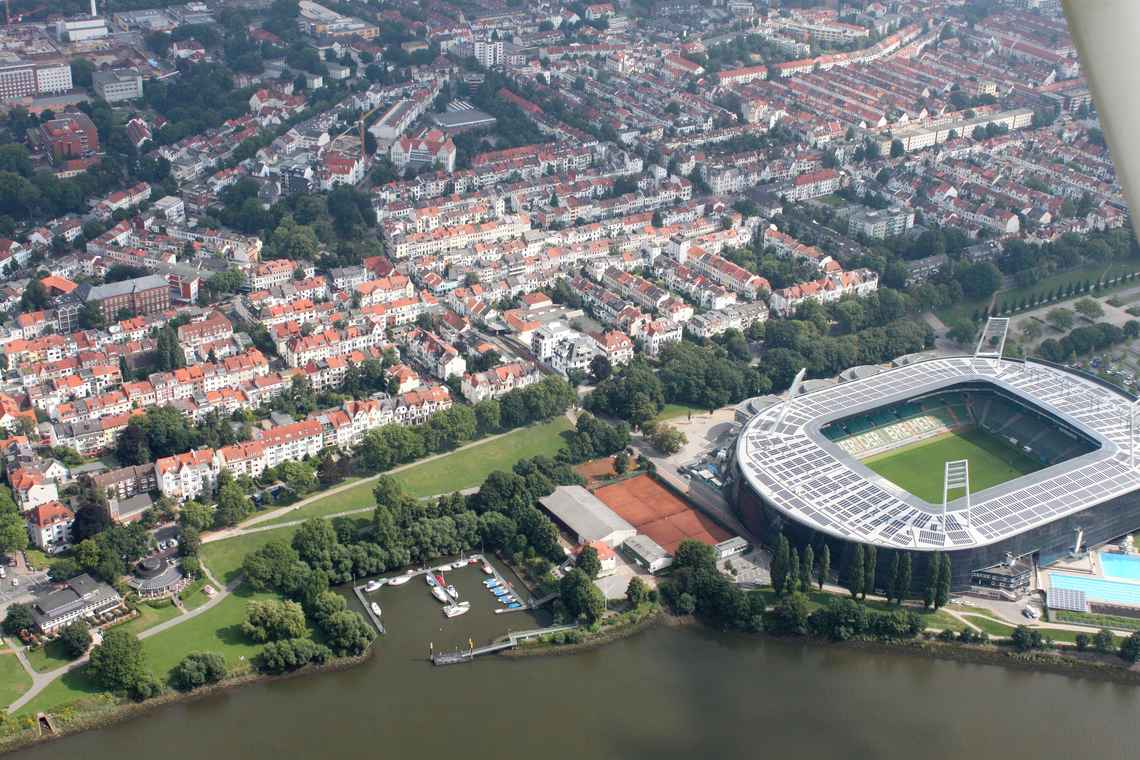Vista aérea de una ciudad con un estadio grande rodeado de edificios residenciales y un río.