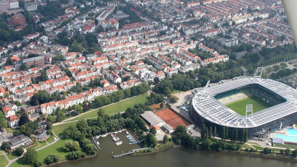 Une vue aérienne d’une ville avec un grand stade entouré d’immeubles résidentiels et traversée par une rivière.