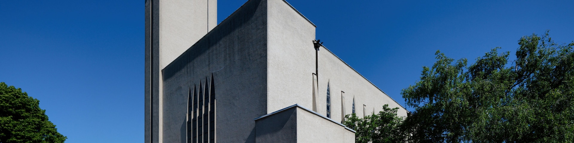 Una iglesia grande con una torre alta y un reloj, rodeada de árboles y un área pavimentada con escalones que conducen a la entrada.