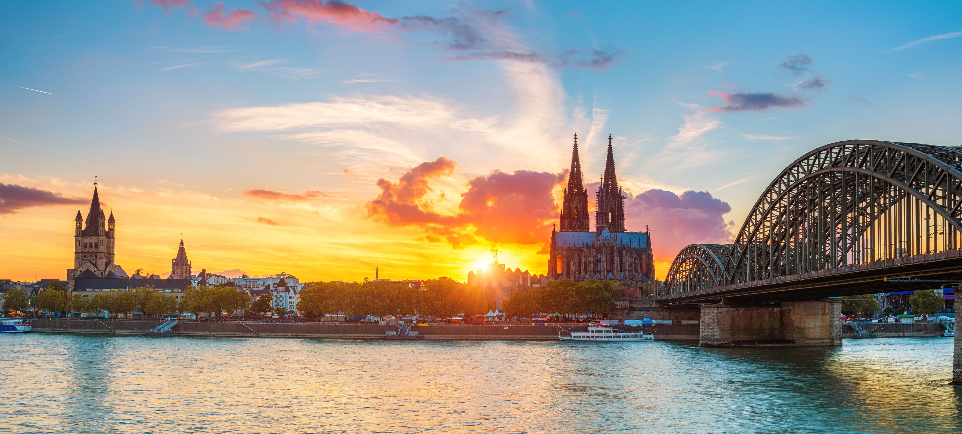 A sunset over a city with two prominent cathedrals and a large bridge.
