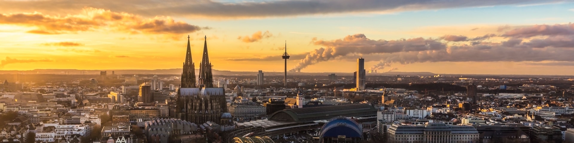 Eine Stadtansicht mit einem markanten Dom, einem Turm und einer Brücke mit beleuchteten Kabeln.