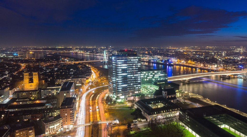 A nighttime cityscape with illuminated buildings, a river, and a bridge.