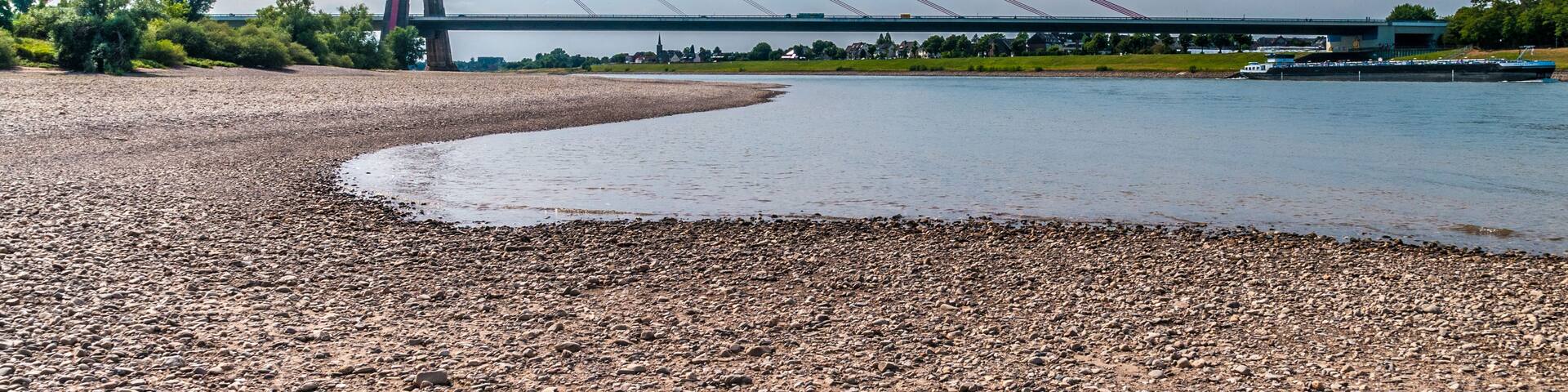A cable-stayed bridge over a river with pebbly shore and a clear sky.