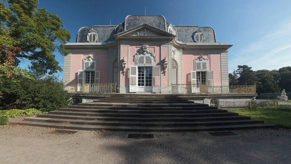 A pink and white building with a grand entrance, steps leading up to it, and a statue in front.