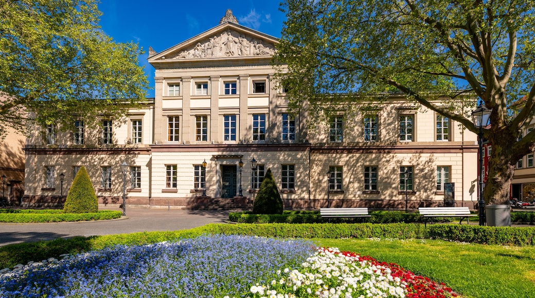 En klassisk bygning med en midterindgang, omgivet af en velplejet have med et væld af blomster.