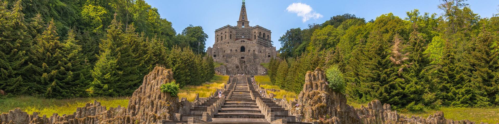 A historic stone structure with a central tower, surrounded by a moat and dense forest.