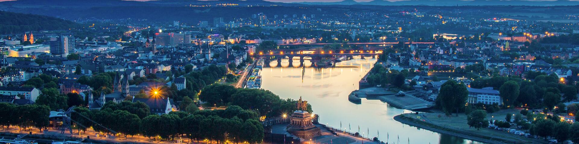 A cityscape at dusk with a river, a bridge, and a statue.