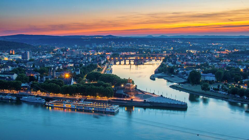 Een stadsgezicht in de schemering met een rivier, een brug en een standbeeld.