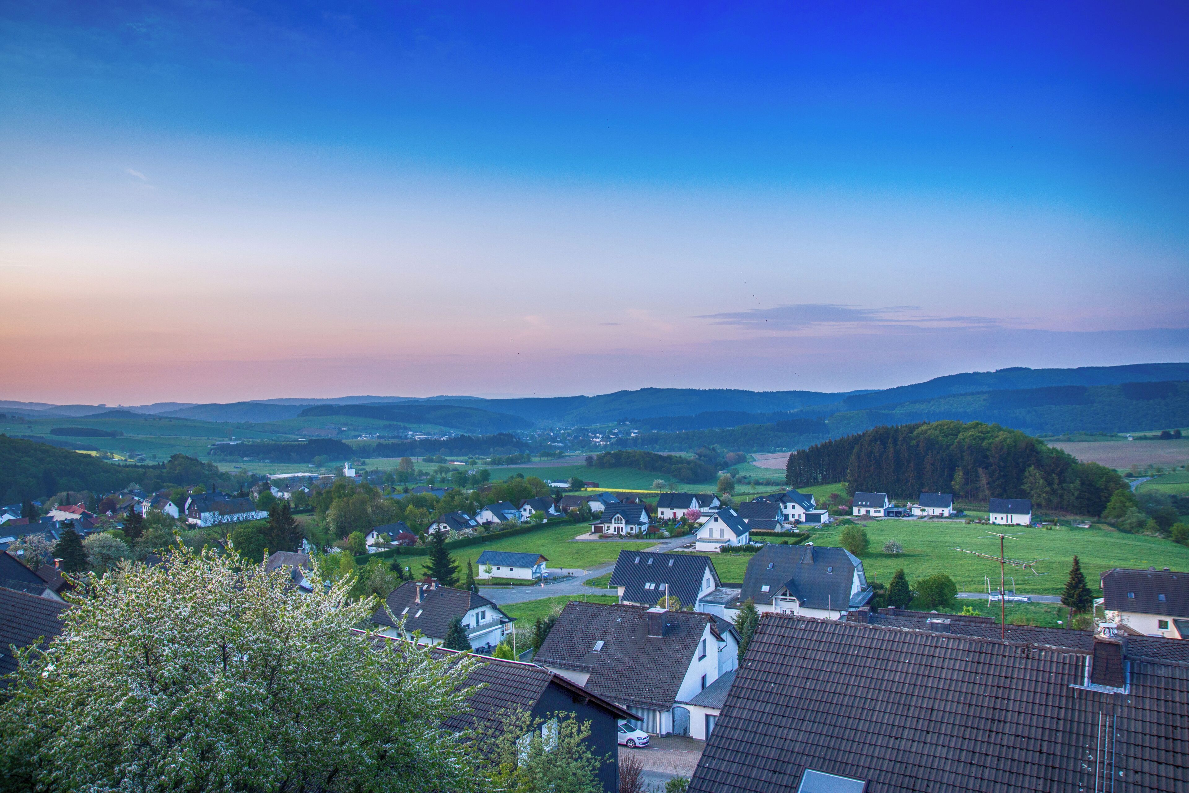 A rural village with houses, green fields, and rolling hills in the background.