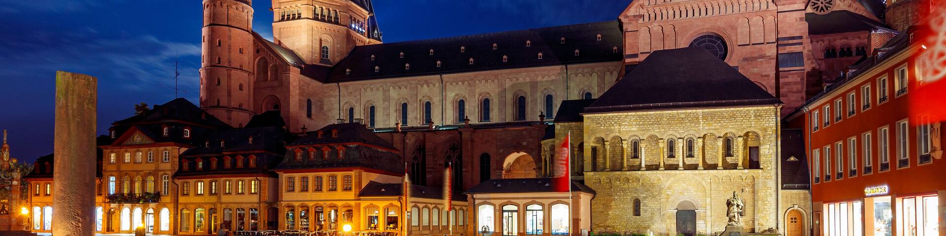 A historic building with multiple towers and a large clock tower, illuminated at night.