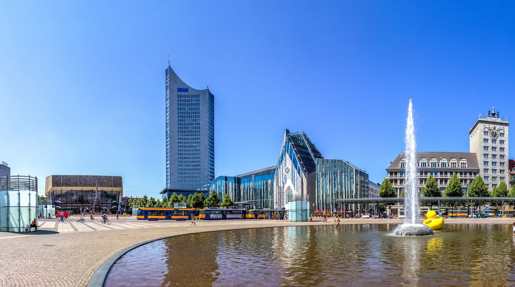 A city square with a fountain, modern buildings, and a historic clock tower.