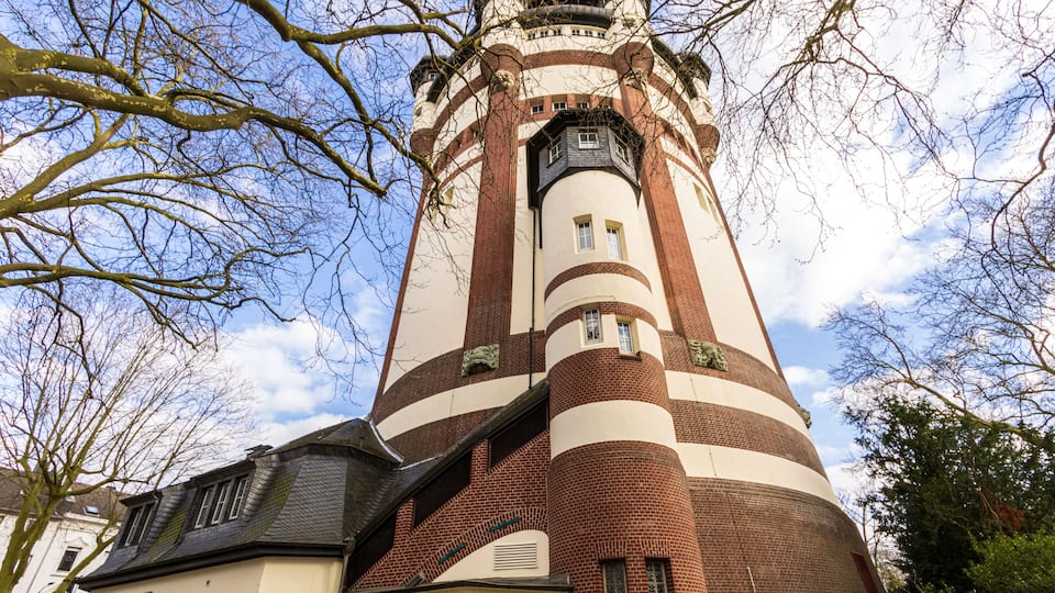 A tall brick tower with a white facade, surrounded by trees and a clear sky.