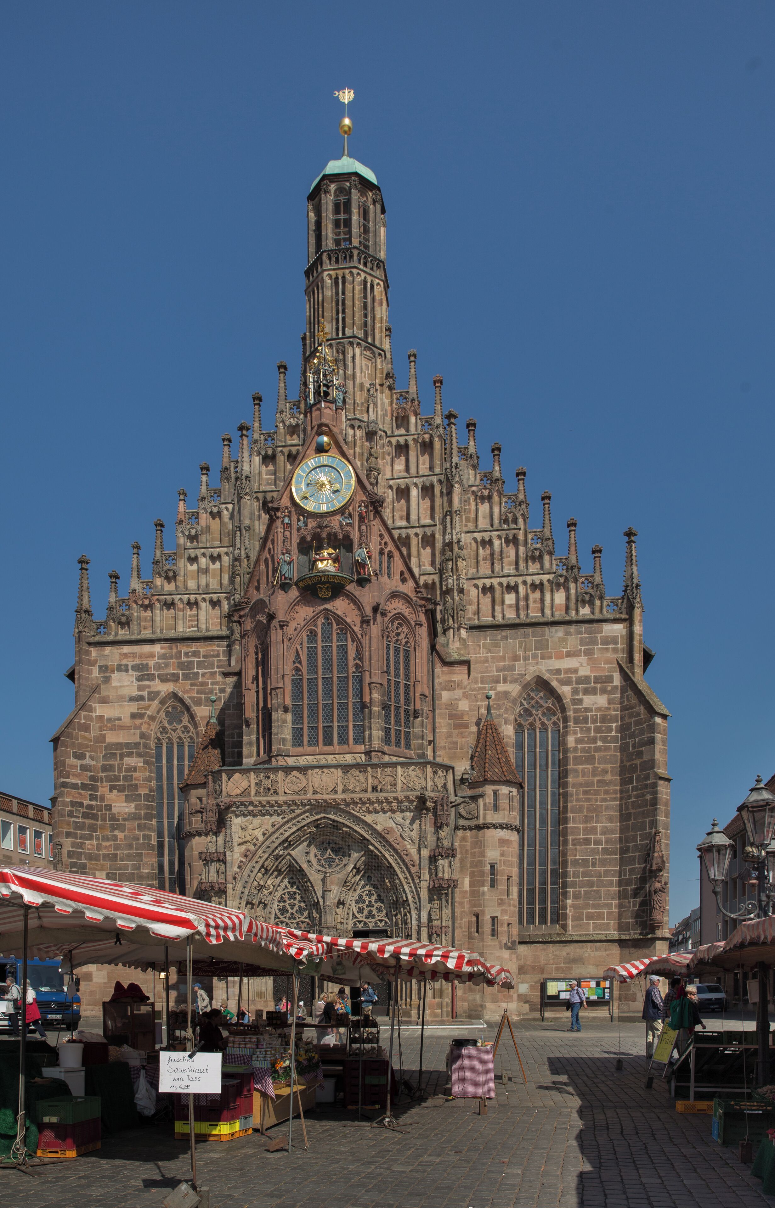 En historisk katedral med et tårn, markedsboder og en klar blå himmel.