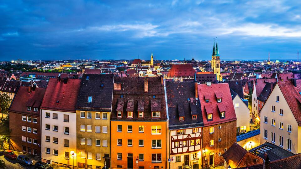 A cityscape with historic buildings, a prominent church tower, and a cathedral with a green spire.