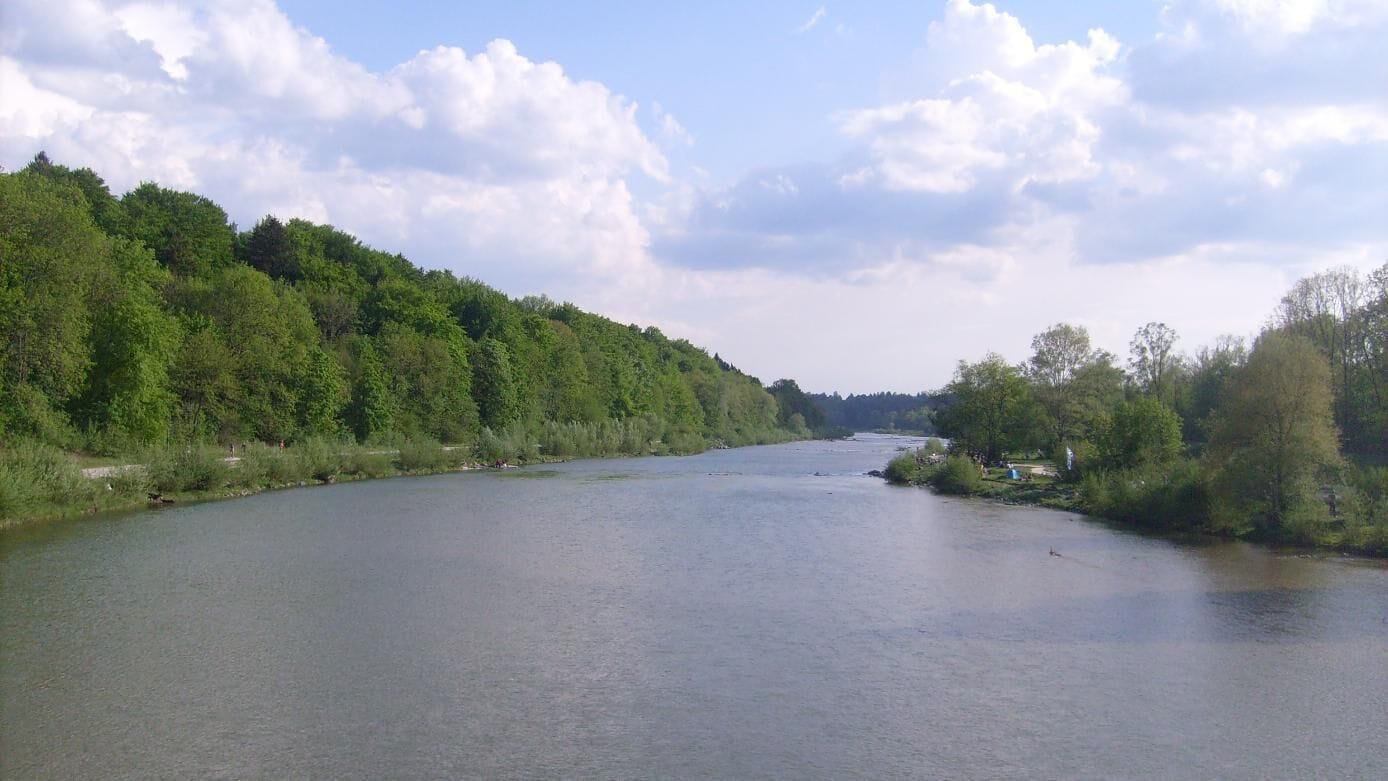 A river flanked by dense green forests under a partly cloudy sky.