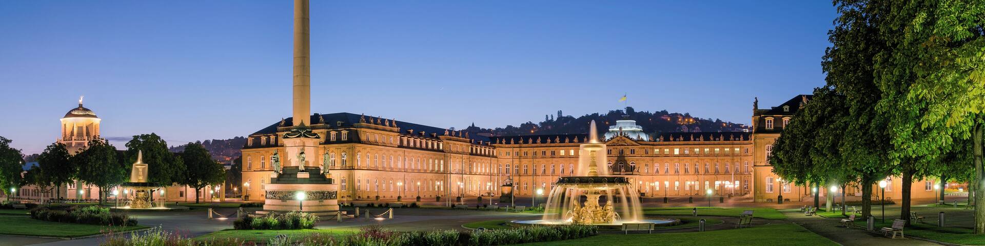 A grand building with a tall obelisk, a fountain, and a well-maintained garden at dusk.