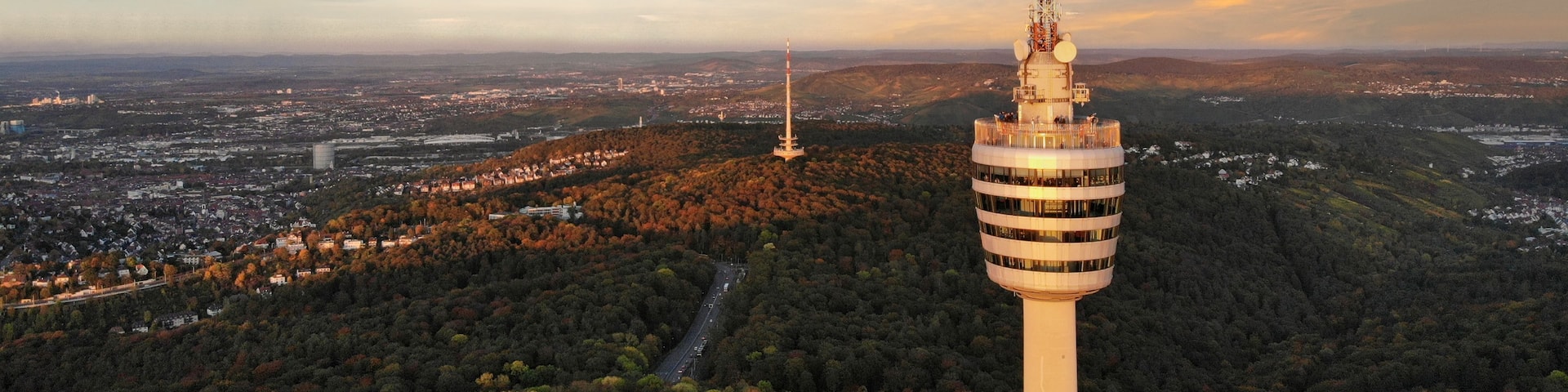 A tower with a spiral staircase, surrounded by a forested area and a cityscape in the background.